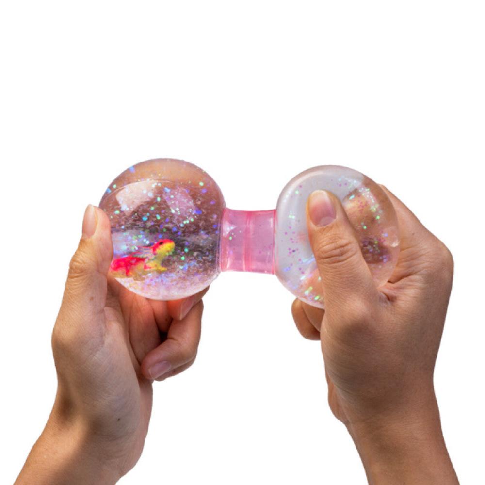 Hands squeeze a clear, glitter-filled fidget toy containing a small colorful figure