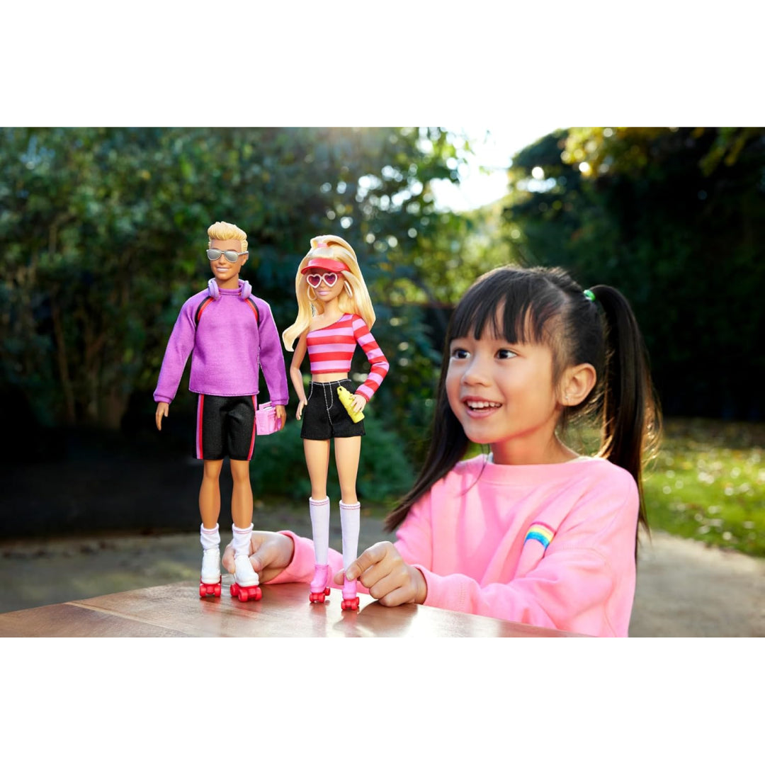Smiling girl looks at Barbie and Ken dolls wearing roller skates on a table outdoors