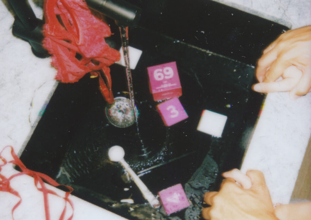 Naughty game for couples with 69 and 3 pink cards a red cloth and two hands in a sink implying playful cleanup