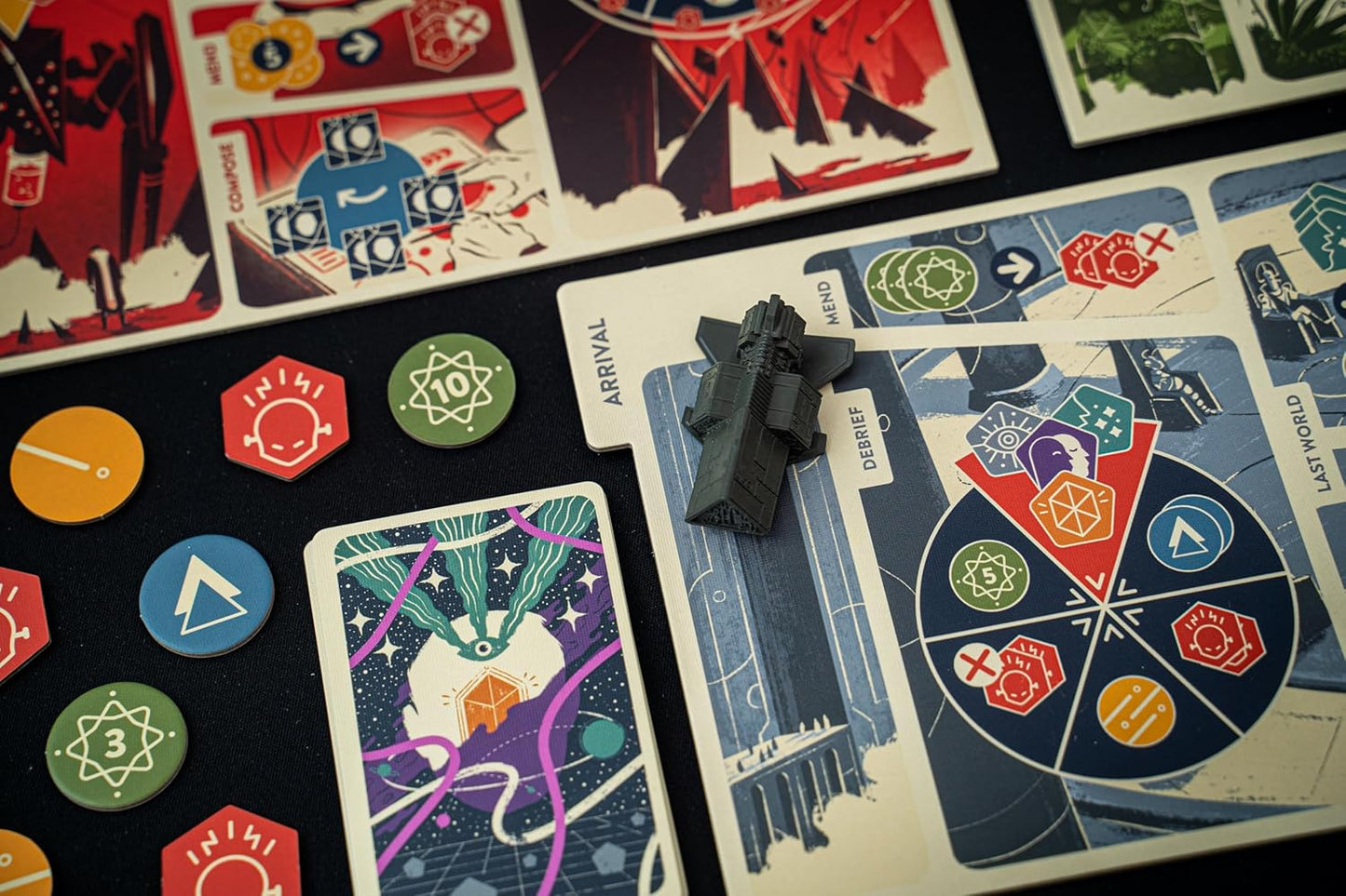 A dark gray spaceship miniature sits on a stylized board game map, surrounded by colorful cards and tokens