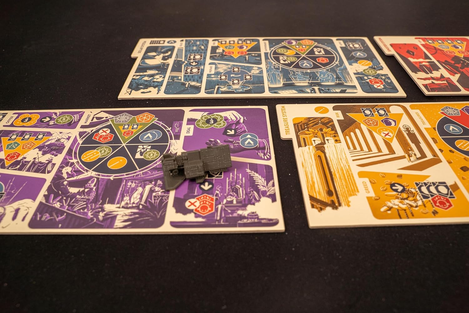 A grey futuristic miniature rests on a purple board game tile. Other blue, red, and yellow game boards are visible on a black table