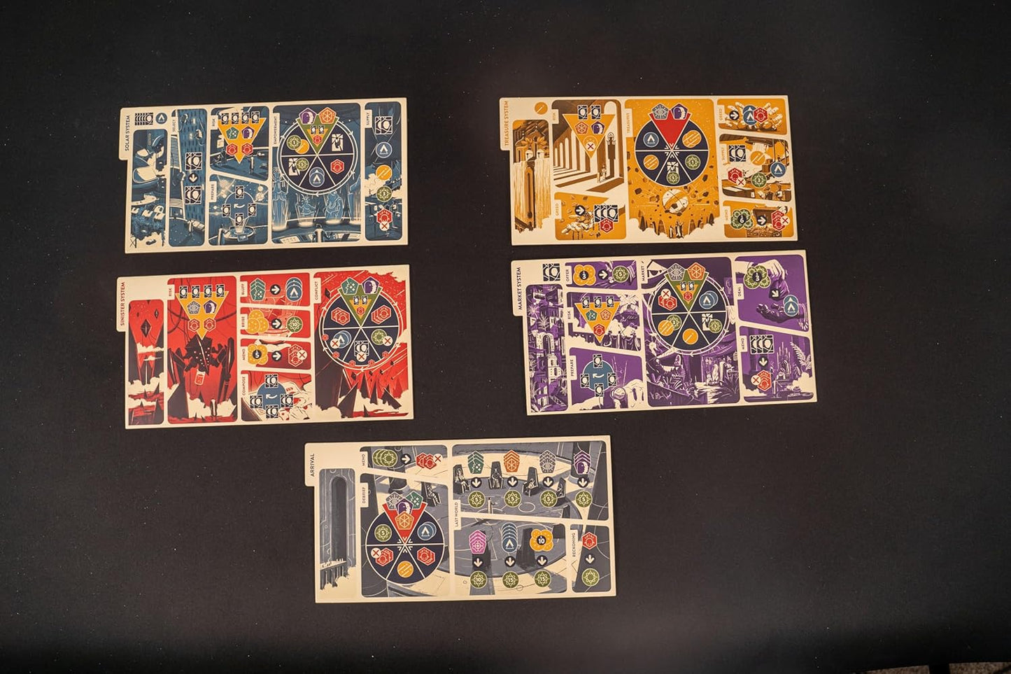 Five distinct board game player mats, each with a unique color scheme and complex icons, arranged on a dark surface