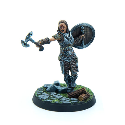 A miniature of a roaring female warrior in armor with war paint, holding an axe and shield on a scenic base