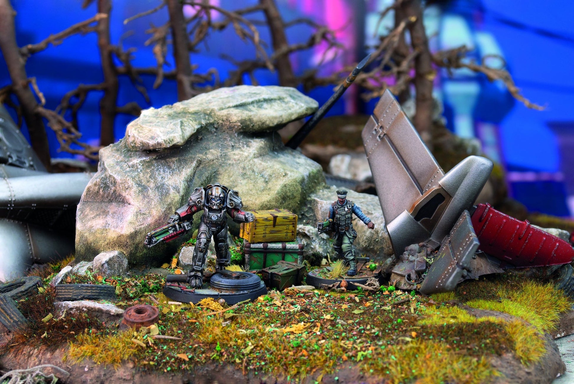 Two detailed miniatures, one armored, one human, in a crash site diorama with debris and crates
