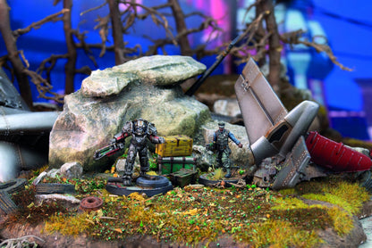 Two detailed miniatures, one armored, one human, in a crash site diorama with debris and crates