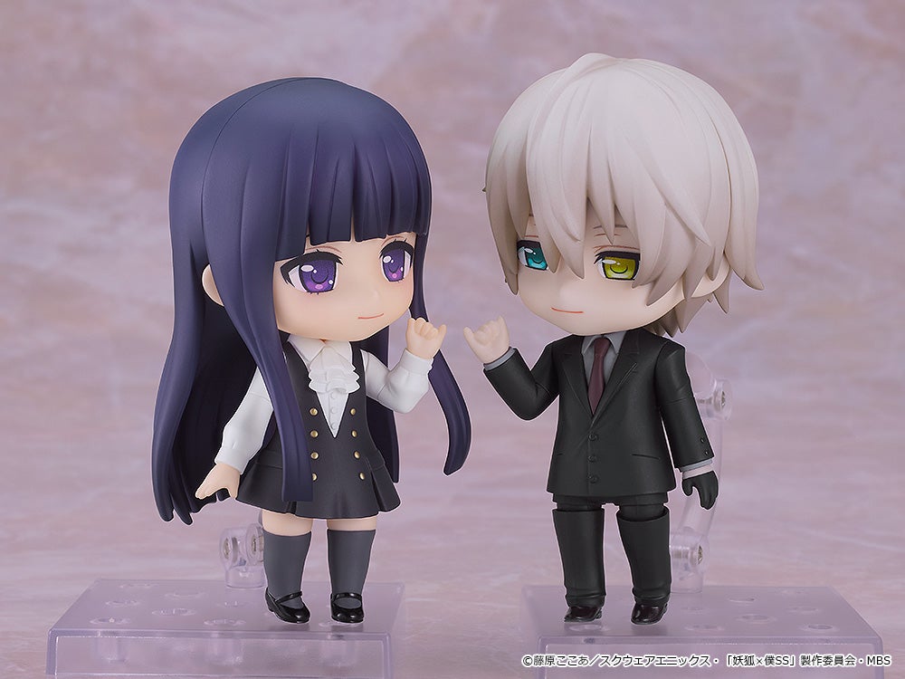 Two chibi figures: a purple-haired girl in a black dress and a white-haired boy in a dark suit with heterochromatic eyes, both raising a hand in greeting.