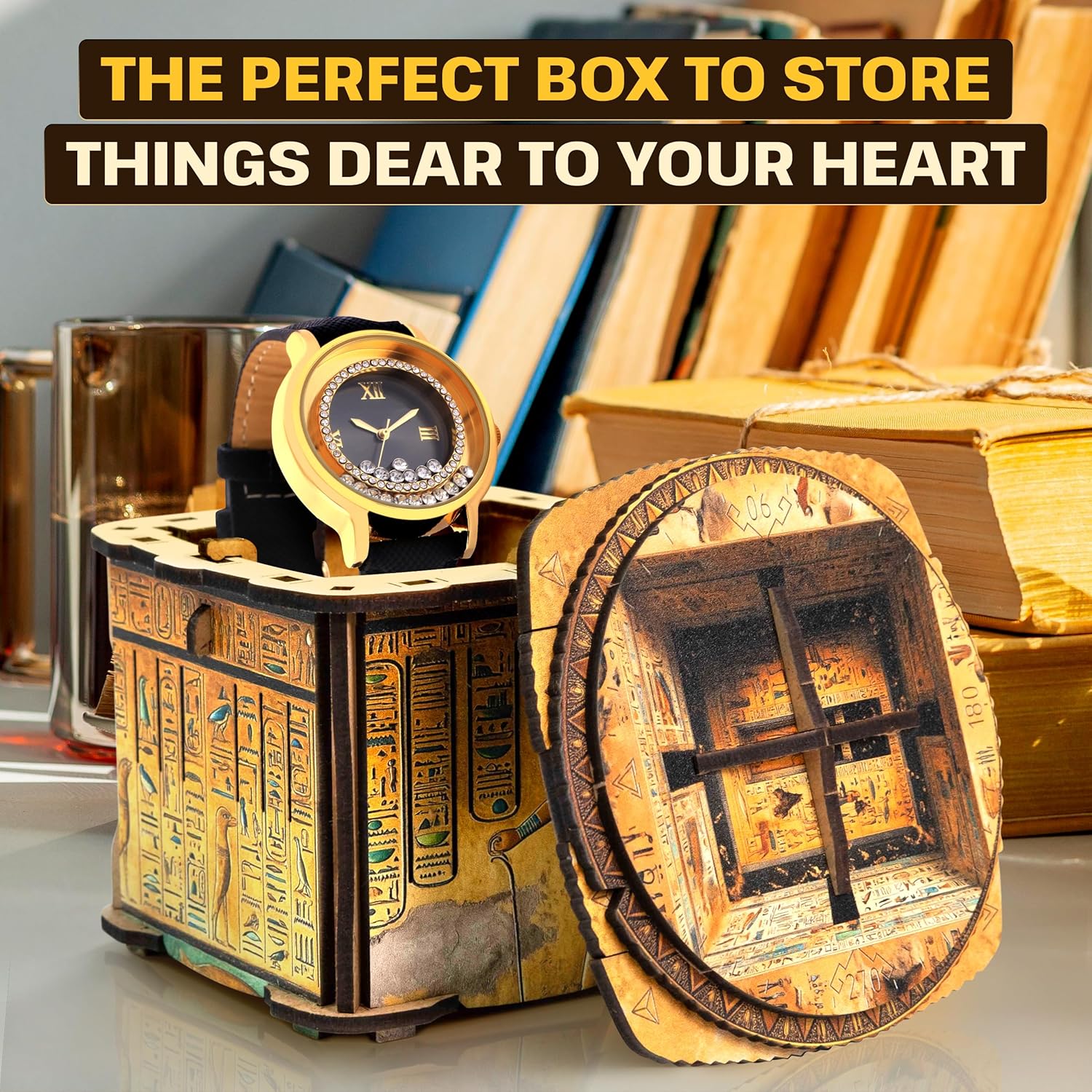 An open ornate wooden box with Egyptian hieroglyphs displays a gold watch, its lid showing a tomb interior.