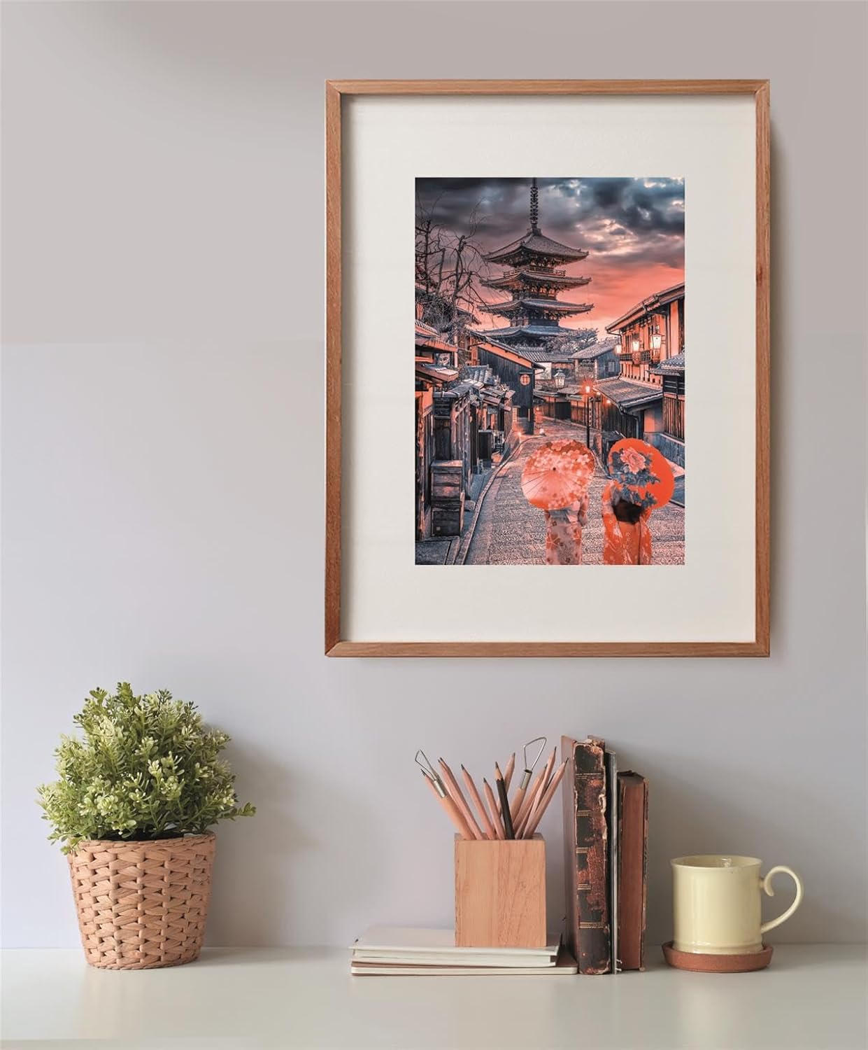 A framed photo of a Japanese street with a pagoda and two people with umbrellas at sunset, above a desk.