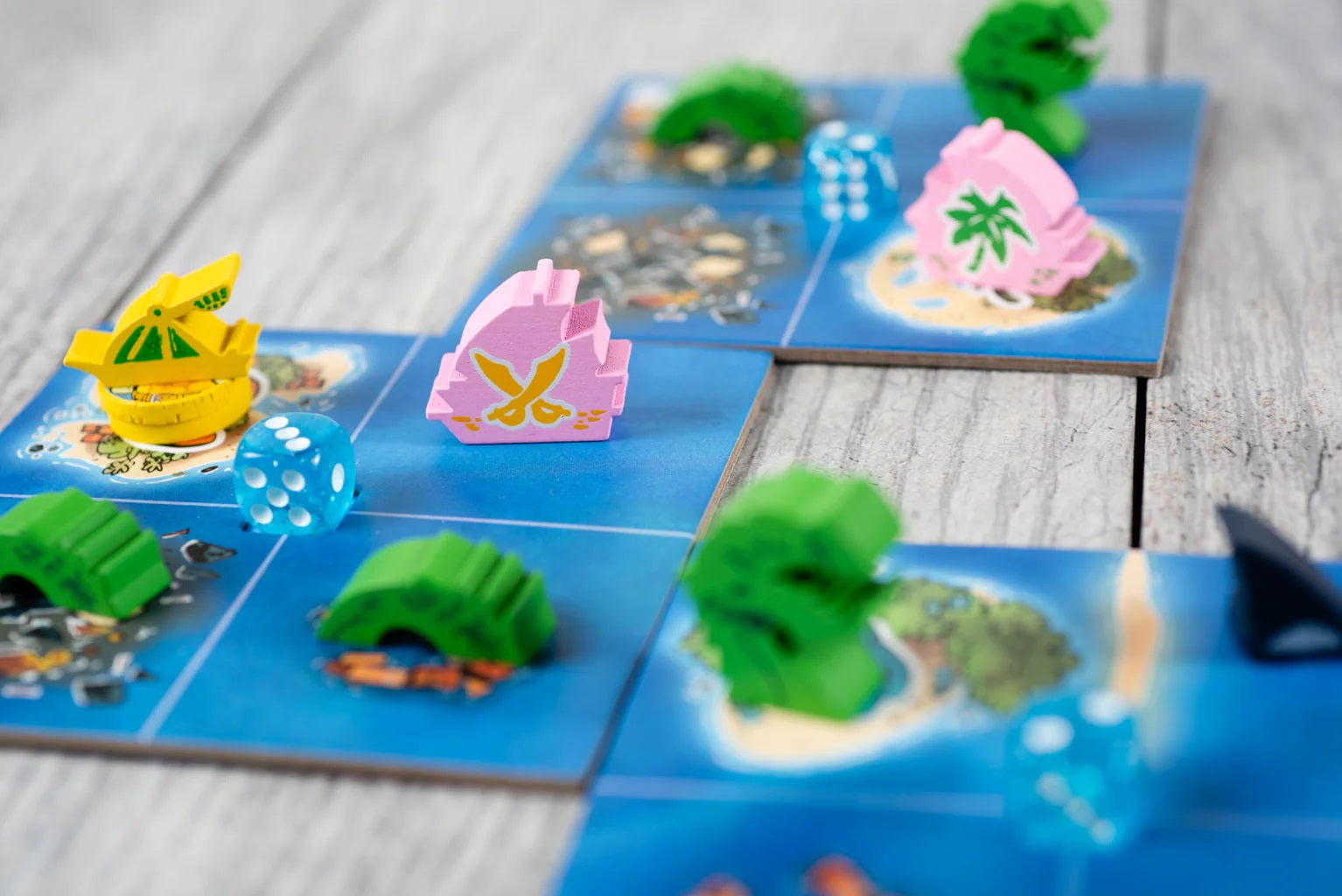 Close-up of pink and yellow wooden ships and a blue die on modular nautical board game tiles