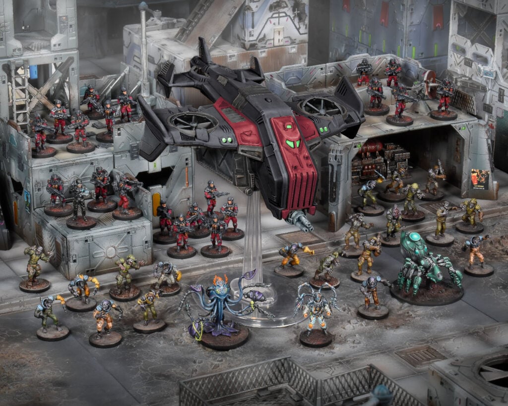 A sci-fi wargame display featuring a black dropship, red soldiers and diverse alien miniatures on detailed city terrain