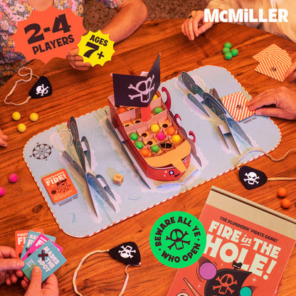 Overhead view of a "Fire in the Hole!" pirate board game in progress, with a ship piece, cards and colorful balls.