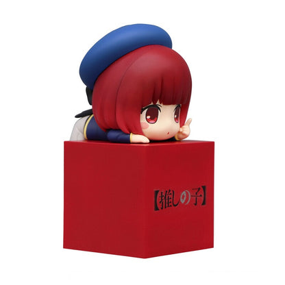 Chibi anime figurine with red hair and blue hat lying on a red cube with Japanese text