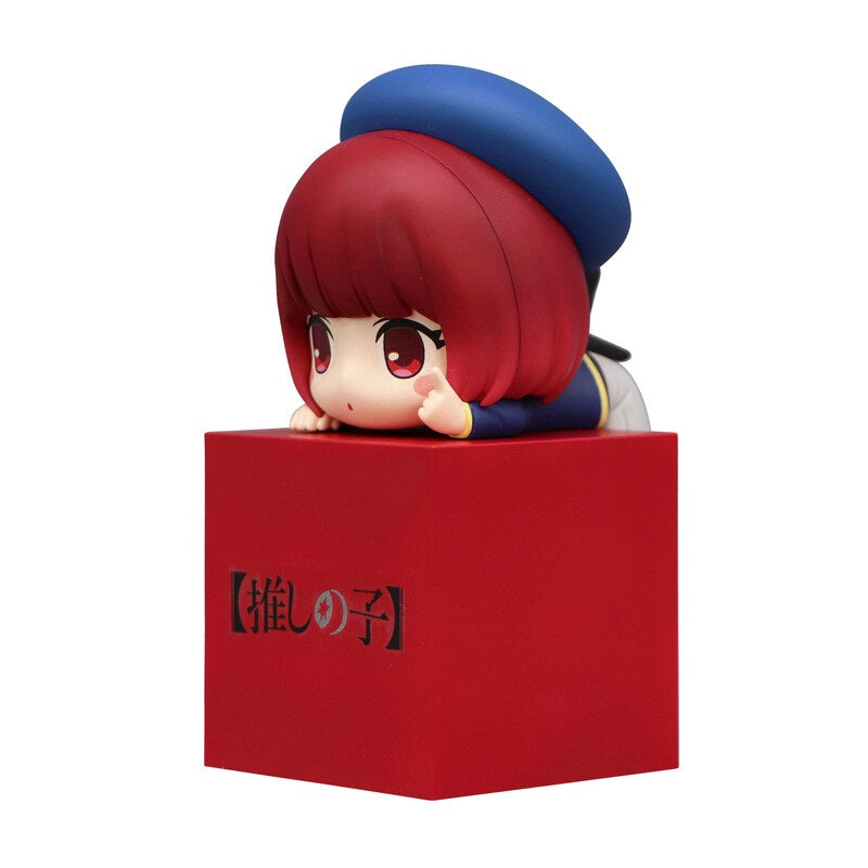 Chibi anime figure with red bob haircut and blue hat lying on a red block with Japanese text