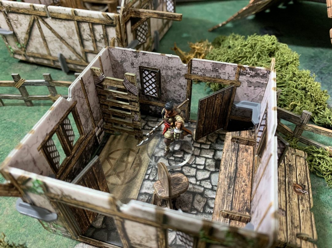 A miniature warrior with a polearm &amp; lantern stands in a modular tabletop building with a stone floor.