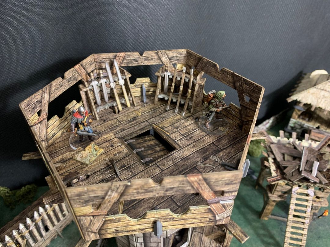 Tabletop RPG scene: Two fantasy miniatures, a warrior on a map and an archer, inside a wooden tower with weapon racks.