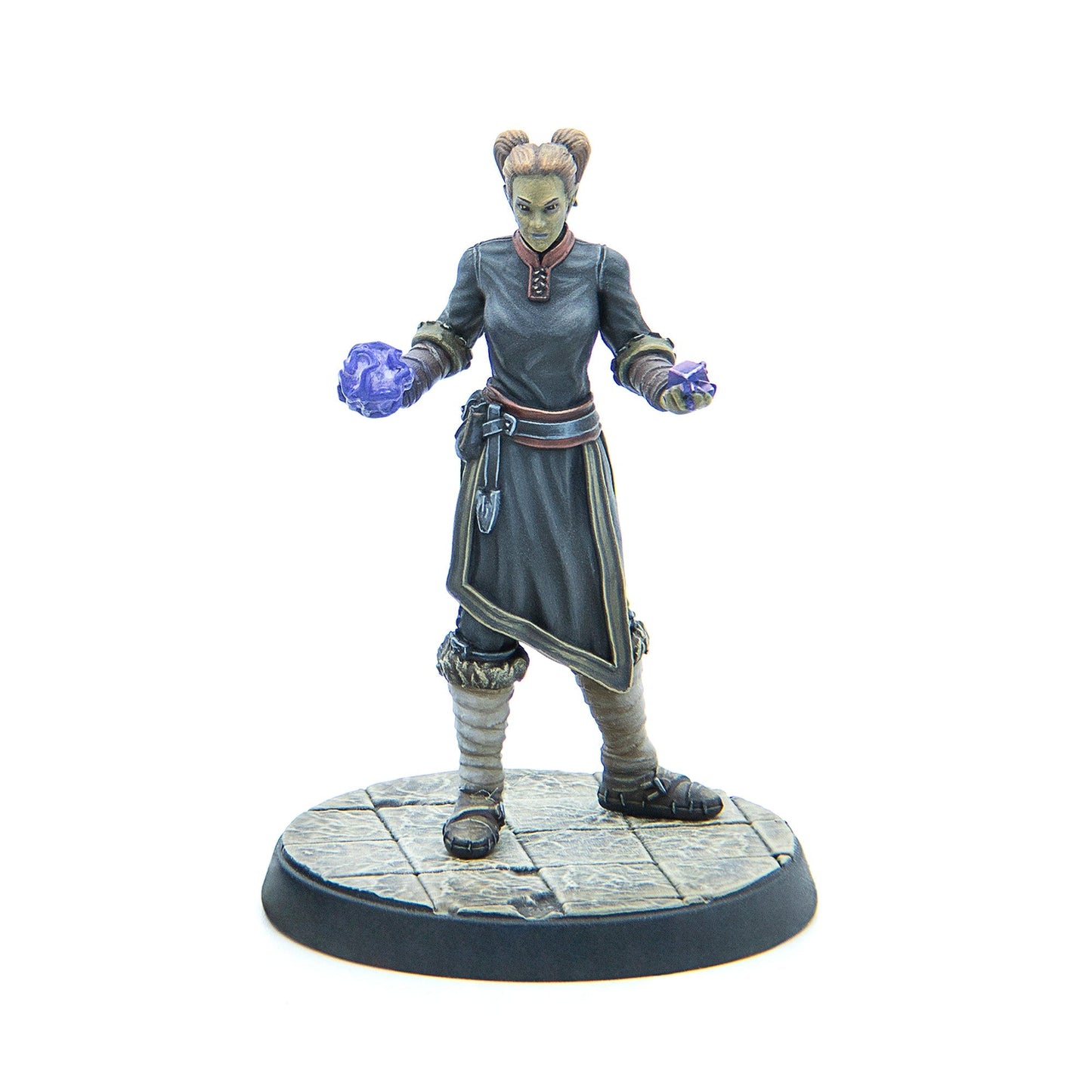A green-skinned female fantasy miniature in dark robes, casting glowing purple magic from her hands, on a tiled base