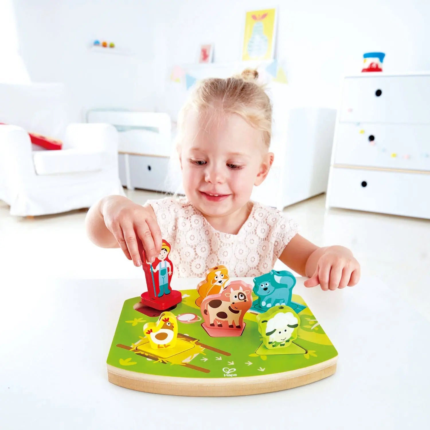 A smiling toddler plays with a wooden farm animal puzzle, placing a farmer figure onto the board.