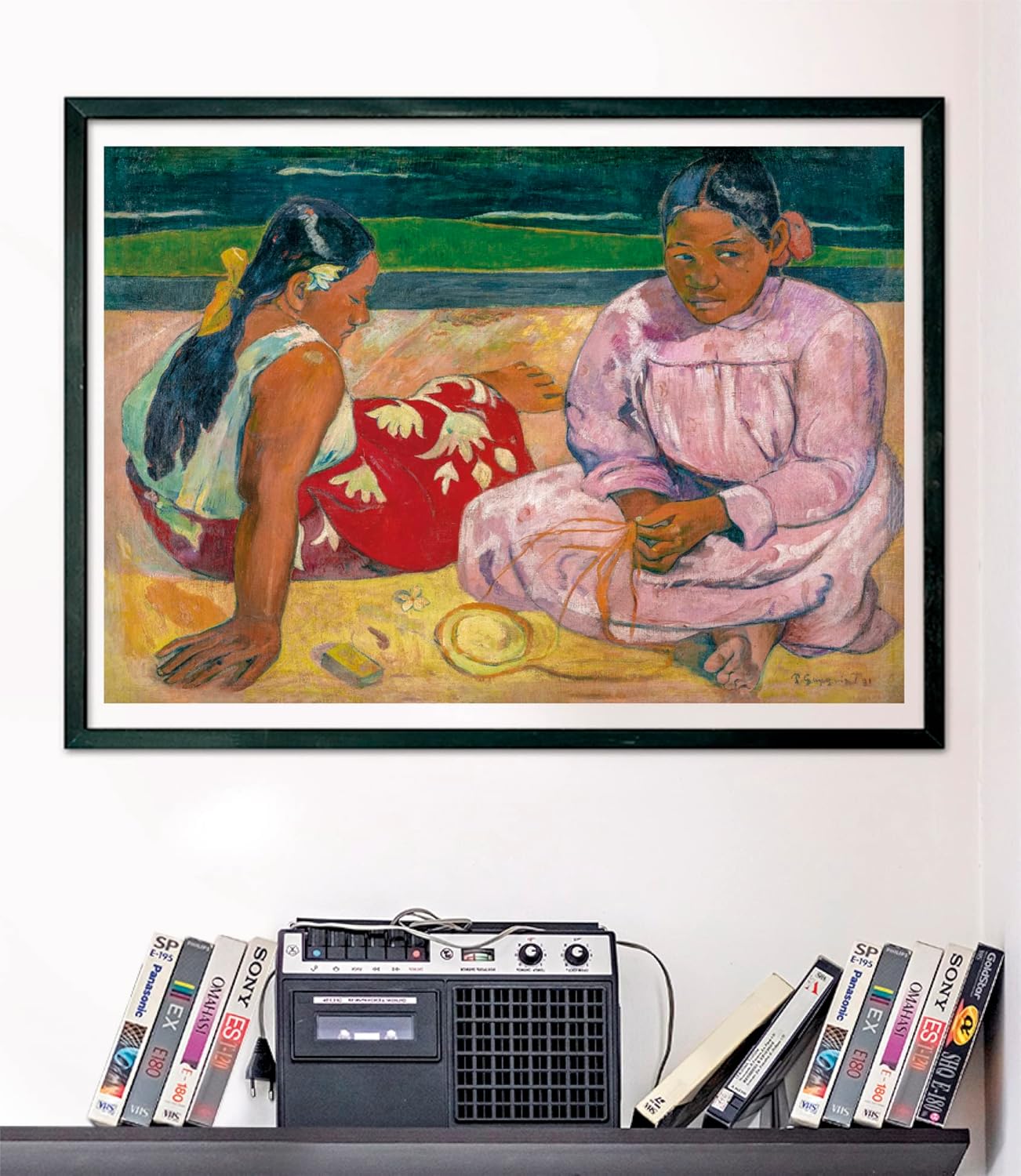 A framed painting of two seated Polynesian women, one looking down, one forward. Below is a shelf with a boombox and VHS tapes