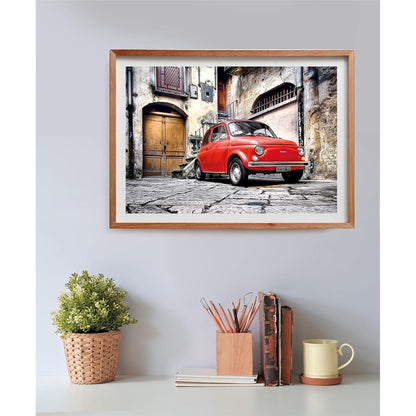 Framed photo of a red Fiat 500 parked on a cobblestone street in front of old European buildings.