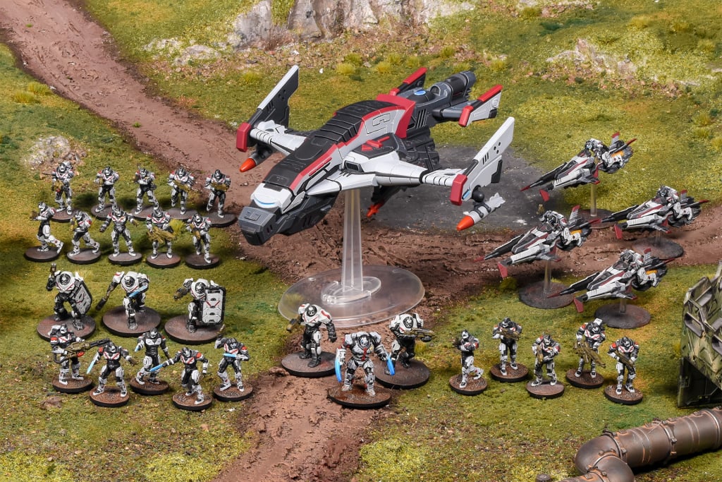 A sci-fi tabletop wargame scene featuring a large dropship, smaller fighters and many armored soldiers on a green battlefield.