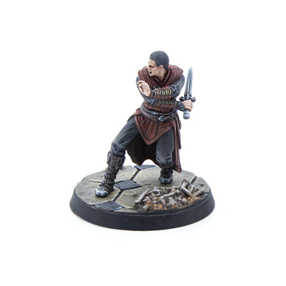 Painted male miniature in dark red and grey robes, wielding a short sword in a dynamic pose on a cracked stone base with bones