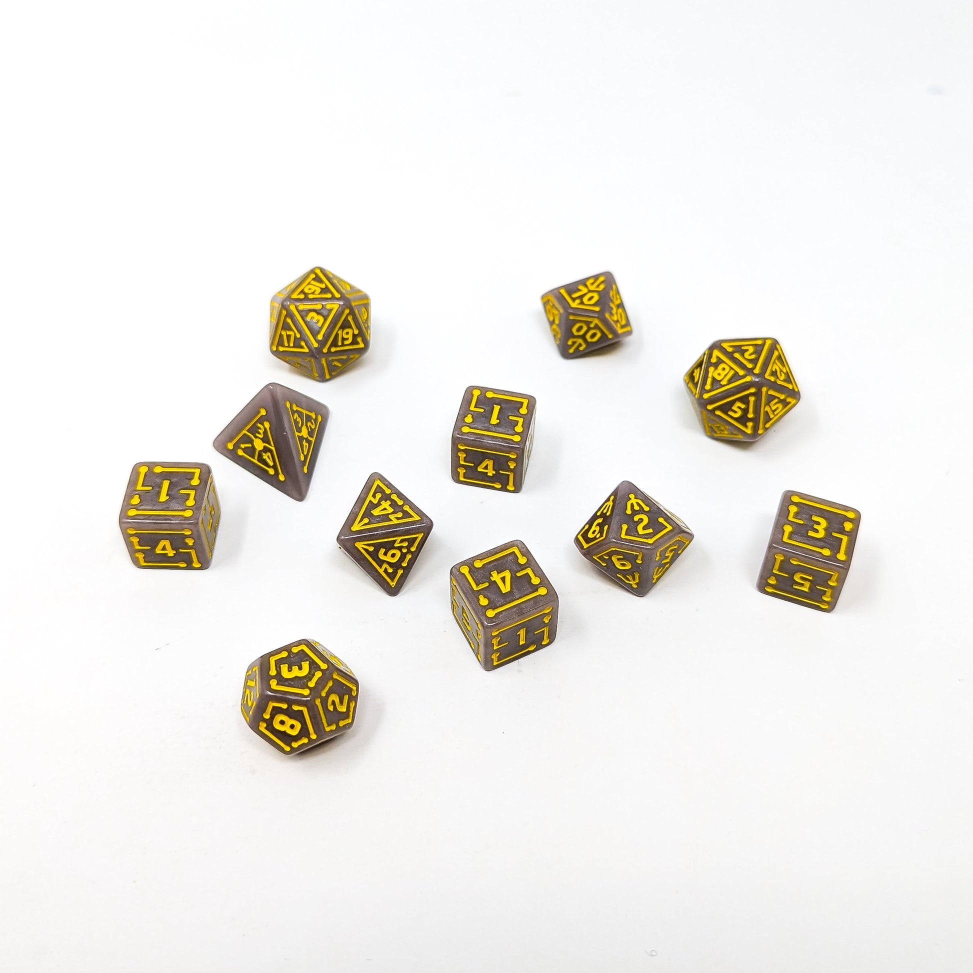 Ten brown polyhedral gaming dice with yellow circuit board-style numbers scattered on a white surface