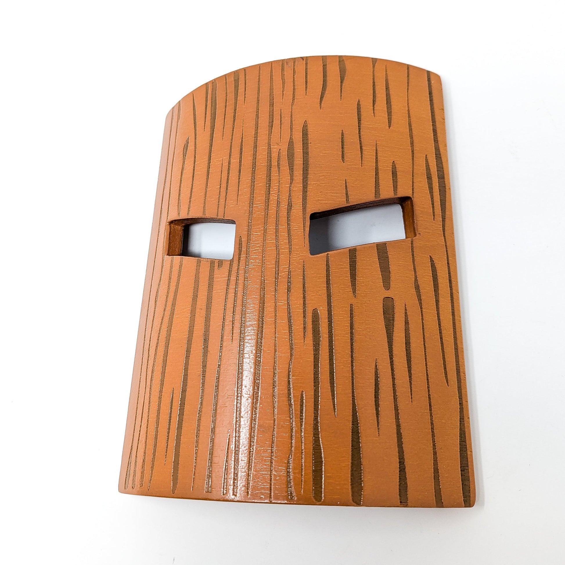 An orange-brown mask with a dark wood grain pattern and two rectangular eyeholes