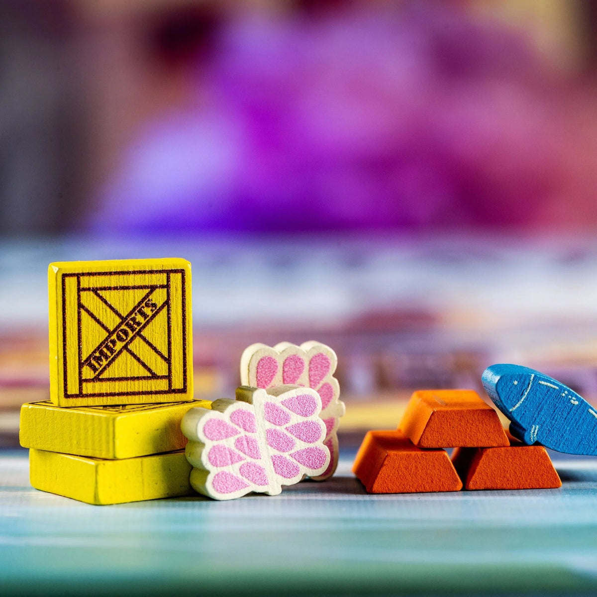 A collection of Yokohama Premium board game tokens features yellow import crates, white and pink silk bundles, orange gold bars, and a blue fish