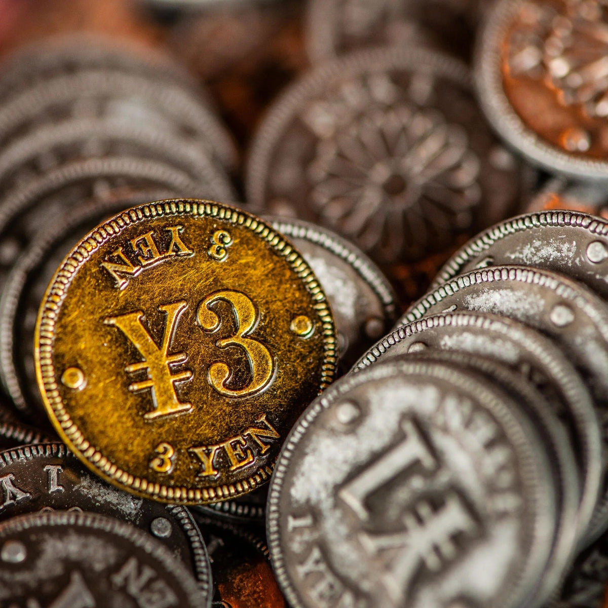 A detailed close-up of Yokohama Premium Tokens, showcasing a golden 3 Yen token with textured surface and ridged edge, nestled among many silver tokens