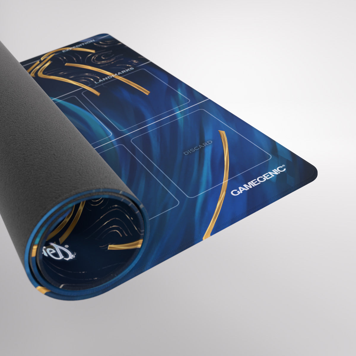 A blue and gold Gamegenic playmat is partially rolled, revealing its textured underside and zones like &#39;DISCARD&#39; and &#39;LANDMARKS&#39;