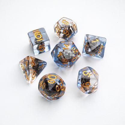Set of 7 translucent blue and clear polyhedral dice with gold numbers, each containing a dark, textured inclusion
