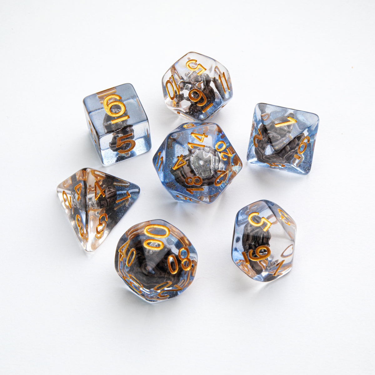 Set of 7 translucent blue and clear polyhedral dice with gold numbers, each containing a dark, textured inclusion