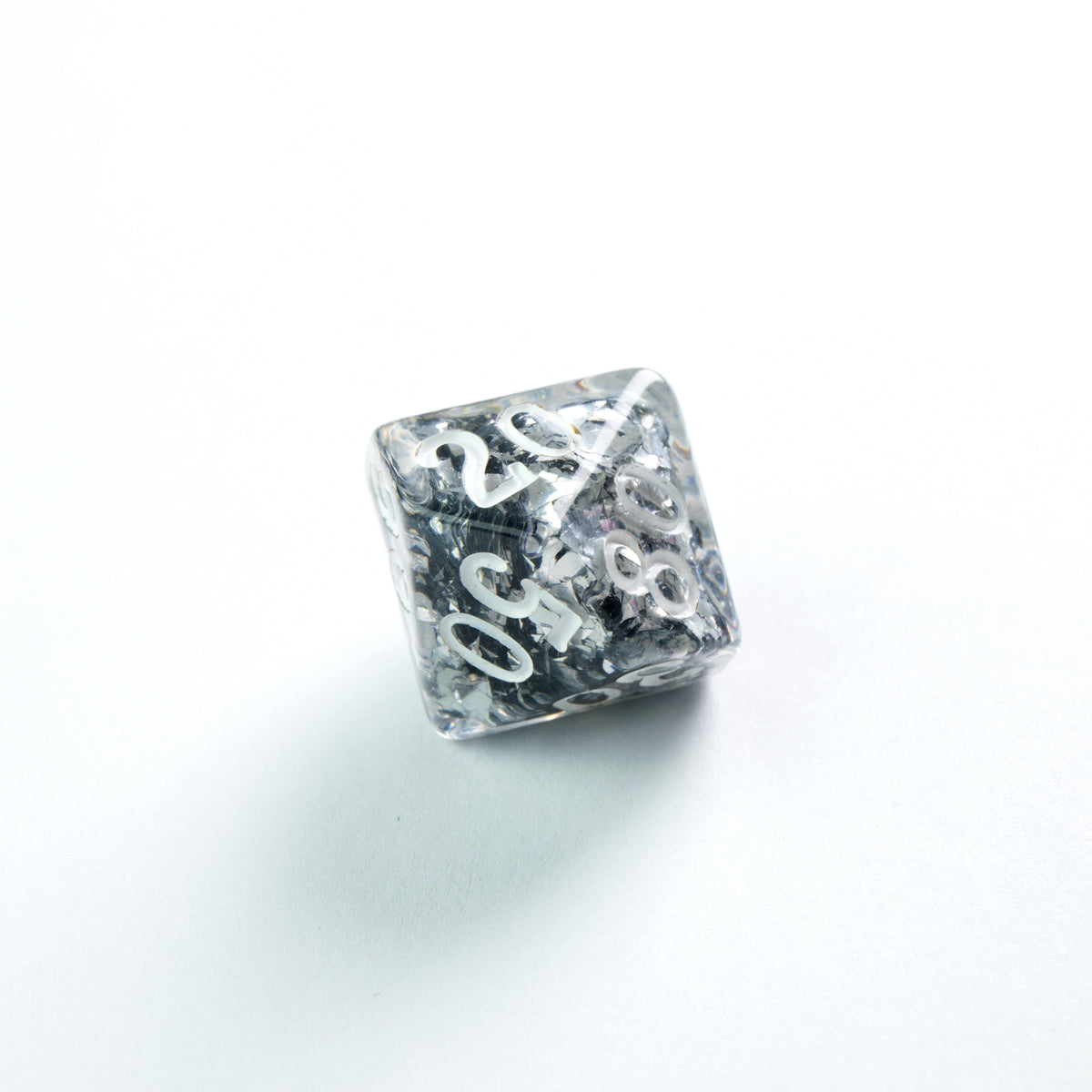 Clear resin polyhedral die with silver glitter inclusions and white numbers, on a white background