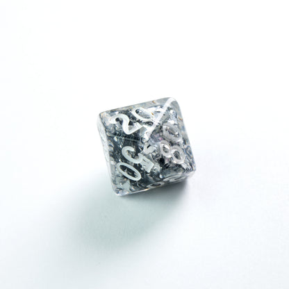 Clear resin polyhedral die with silver glitter inclusions and white numbers, on a white background