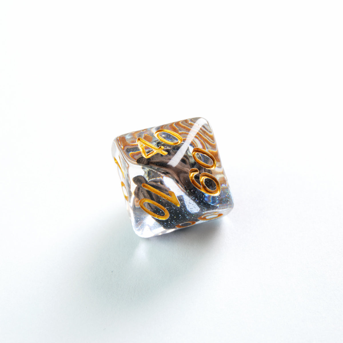 Clear multi-sided die with gold numbers &#39;40&#39;, &#39;60&#39;, &#39;10&#39;, features black glitter and gold swirls inside on a white background