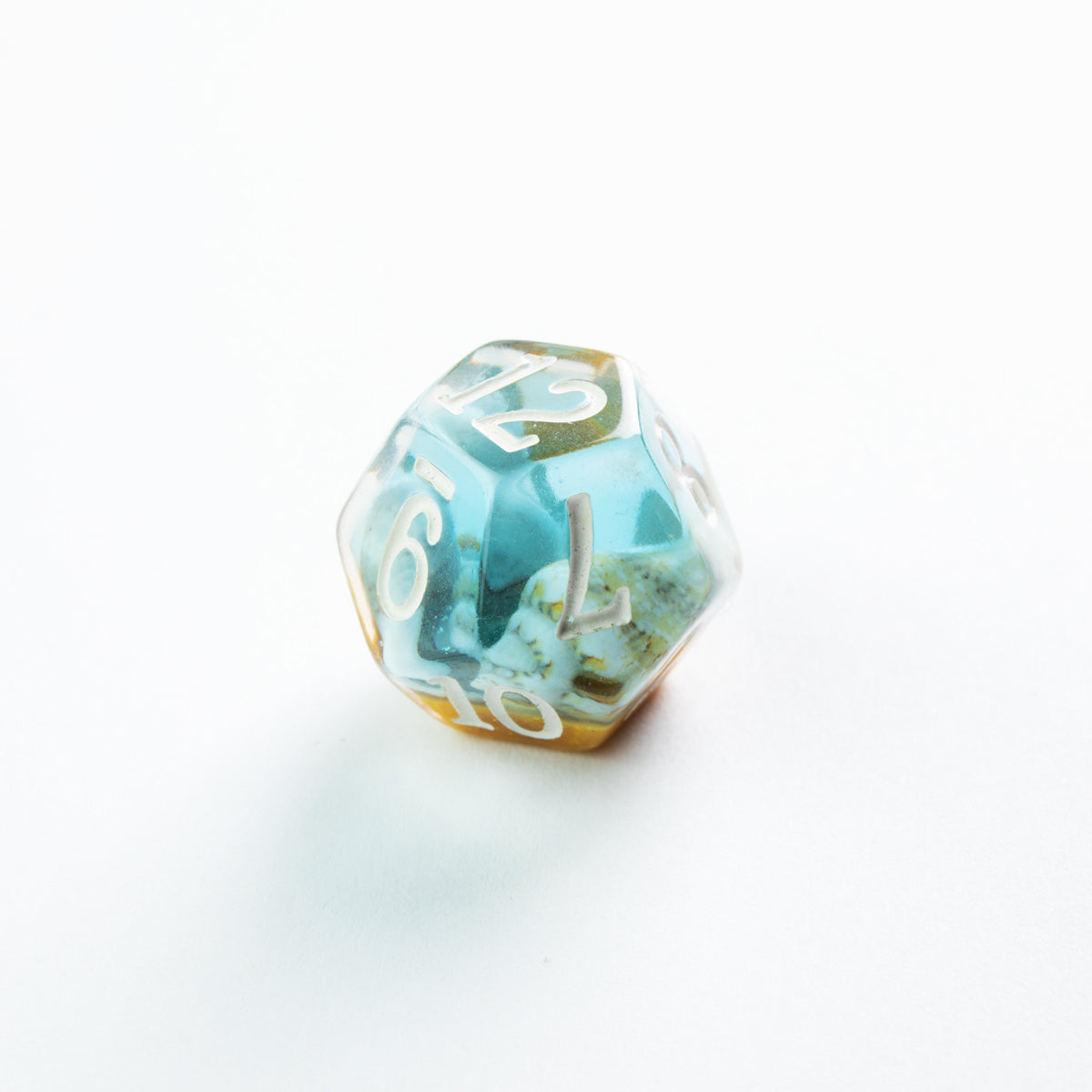 Teal resin D12 die featuring encapsulated shells and sand, resting on a white surface