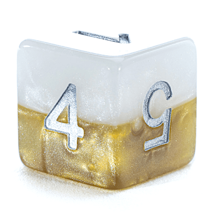 A pearly white and glittery gold gaming die with silver numbers 1, 4, and 5 visible.