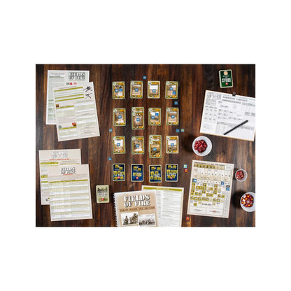 Fields of Fire wargame components laid out on a wooden table, including cards, rulebooks, and tokens