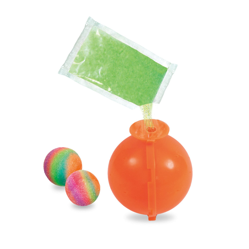 Green powder pours from a pouch into an orange ball mold, alongside two finished rainbow bouncy balls