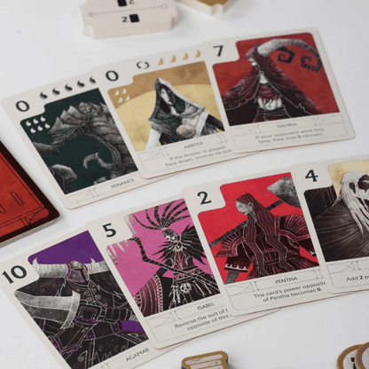 A spread of stylized dark fantasy tabletop game cards showing characters and numerical power values