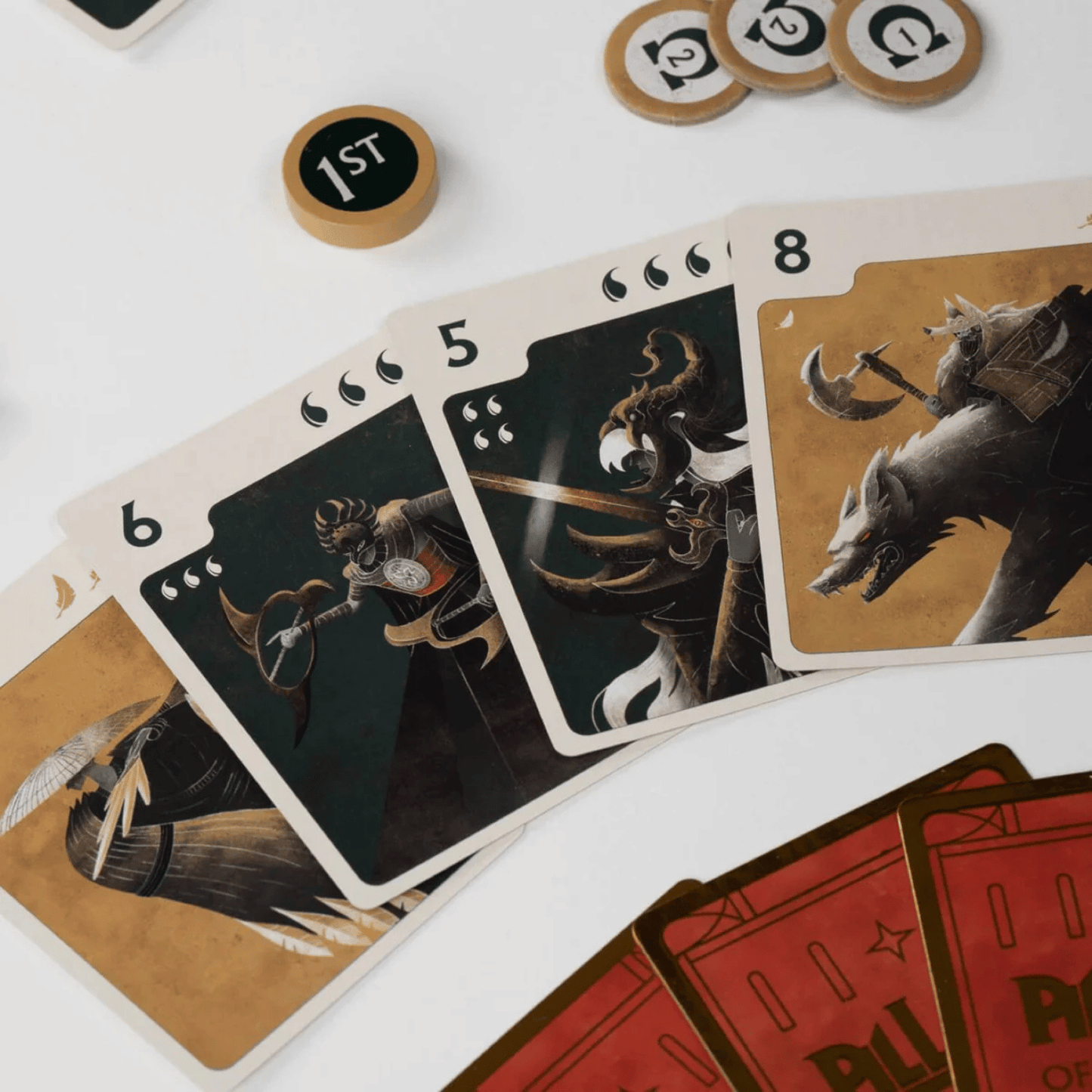 Close-up of fantasy game cards (numbers 5, 6, 8) with warrior artwork, plus tokens including a "1ST" marker