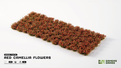 Miniature grass tufts with vibrant red camellia flowers and green bases, arranged on a white surface
