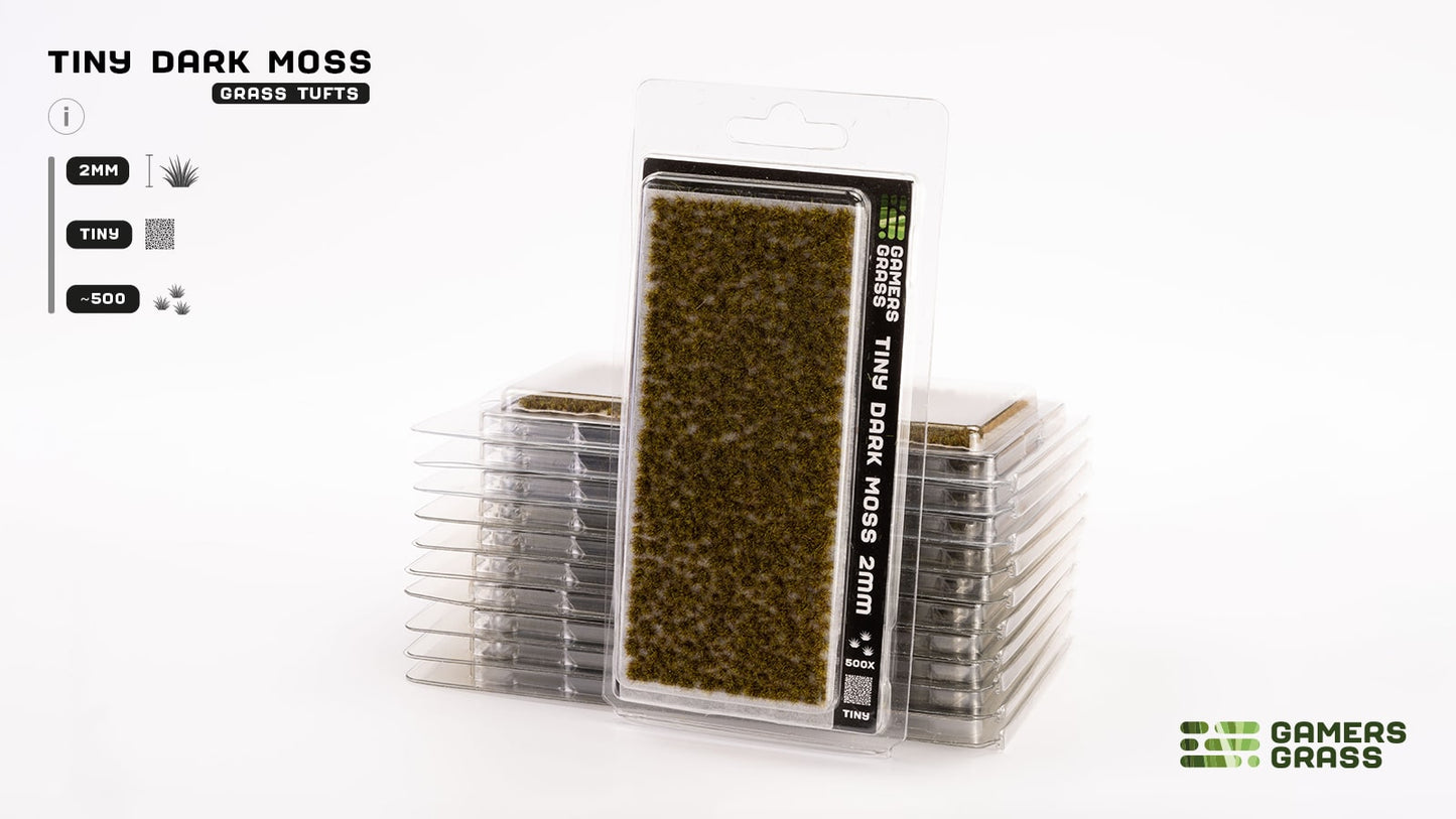 A blister pack of Tiny Dark Moss 2mm grass tufts for models, with more packs stacked behind