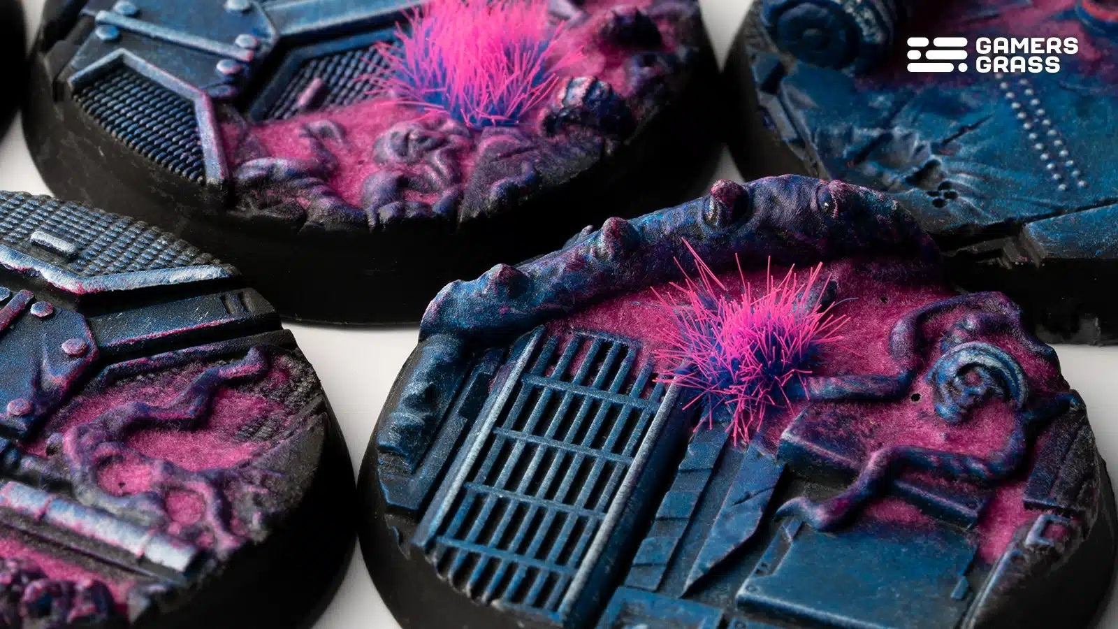 Close-up of sci-fi miniature bases featuring blue industrial structures, textured pink alien ground and neon pink grass