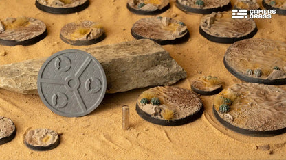 Desert-themed miniature model bases, a gray textured blank base and magnets are displayed on sand