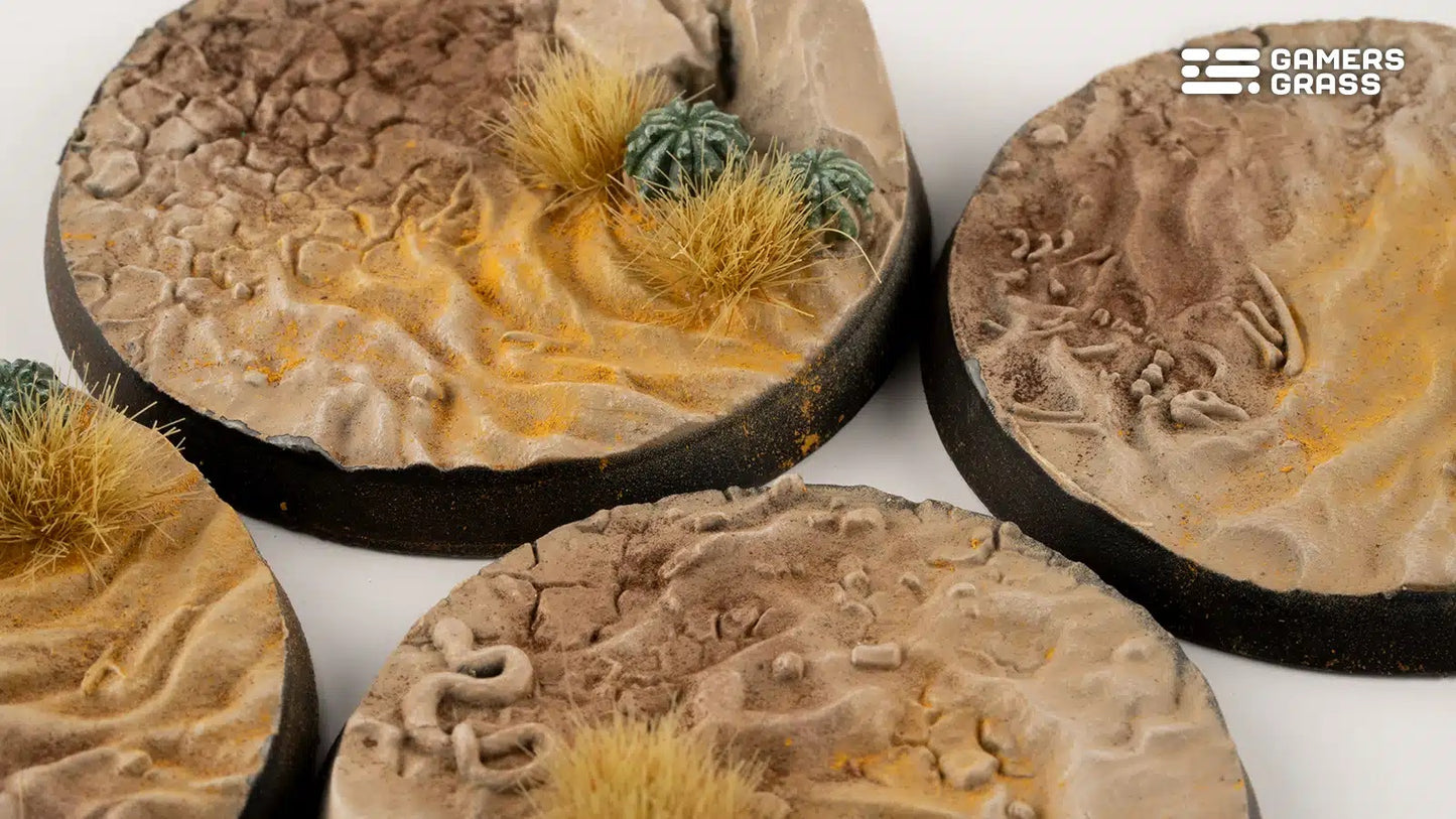Close-up of several detailed, round desert miniature bases featuring sand, dry grass, cacti and subtle terrain elements
