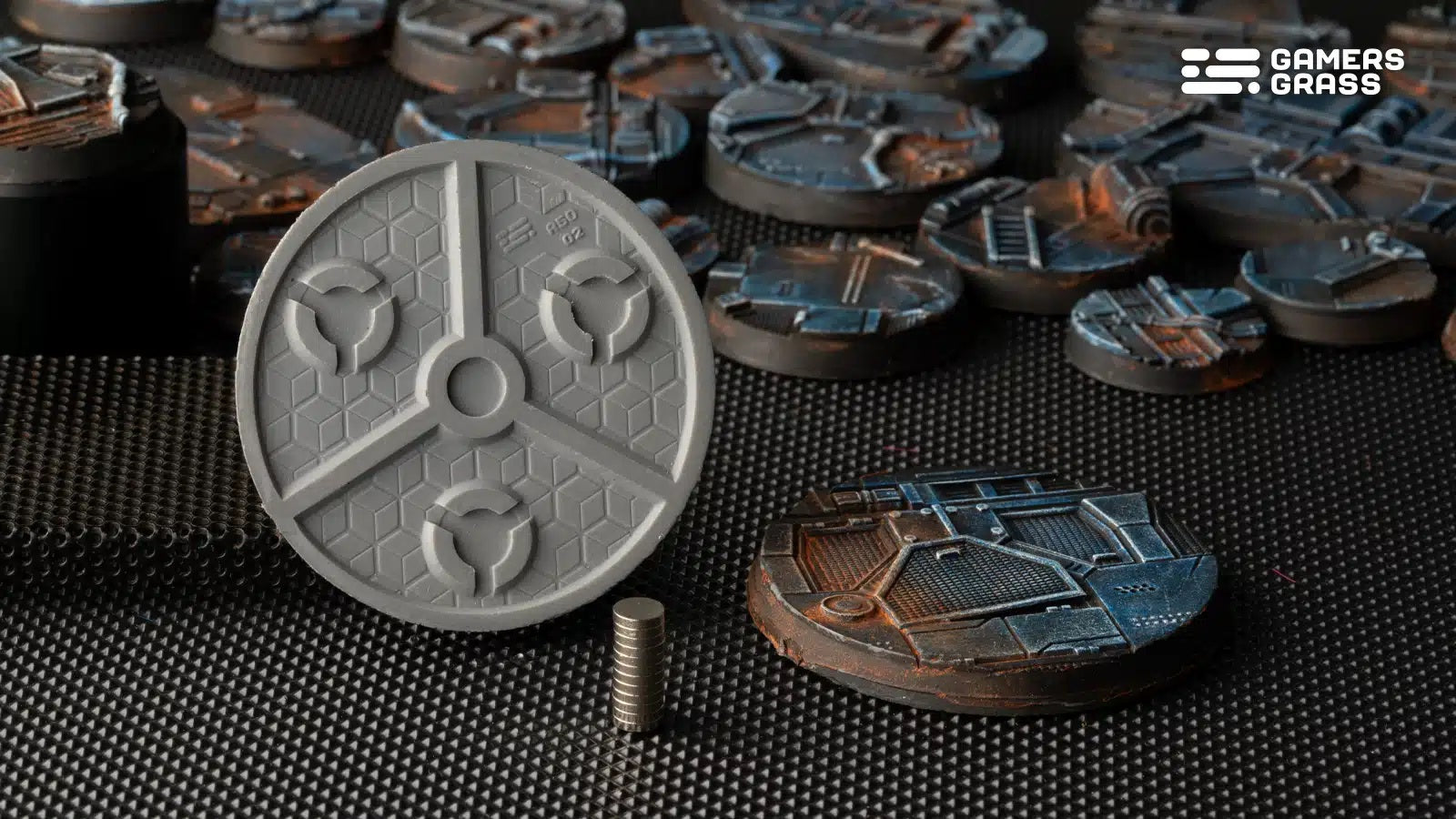 An unpainted gray sci-fi base with magnet recesses, next to a stack of magnets and many finished painted bases