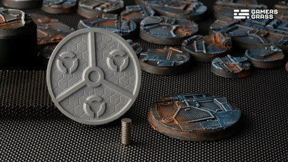 An unpainted gray sci-fi base with magnet recesses, next to a stack of magnets and many finished painted bases