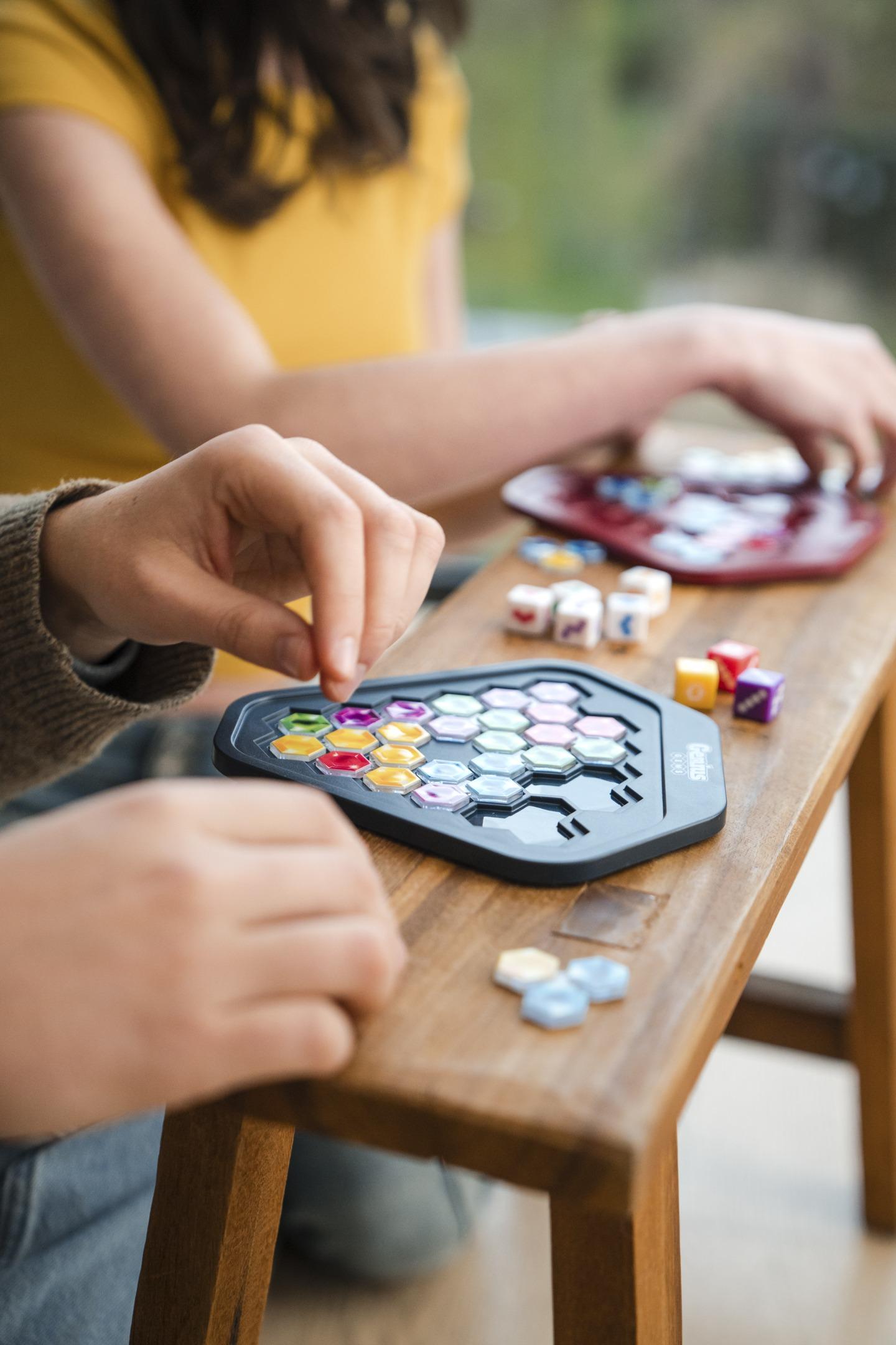 Close-up of hands playing a board game called Genius, placing colorful hexagonal pieces on a wooden table