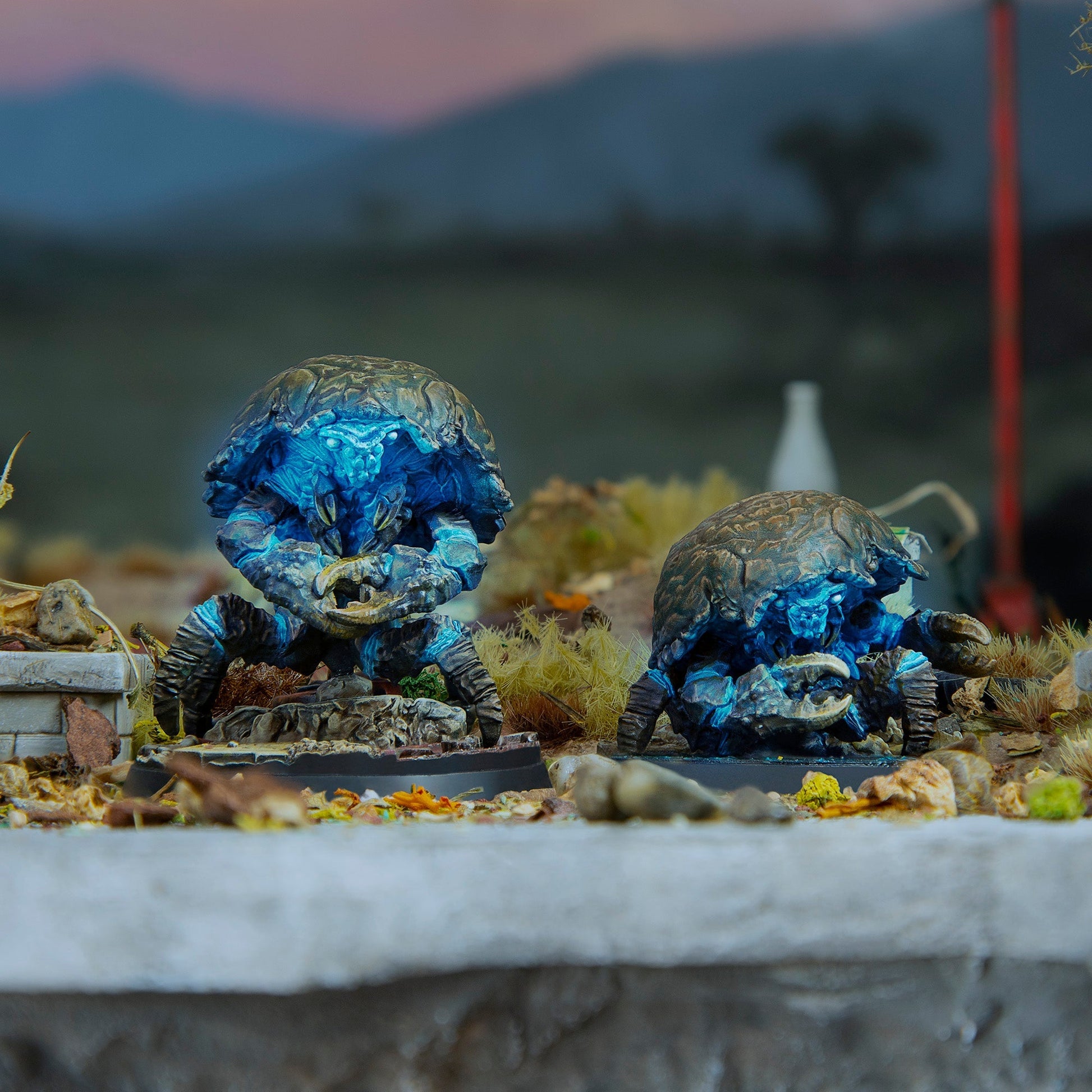Two armored, blue-glowing, crab-like creatures stand on a detailed miniature diorama base